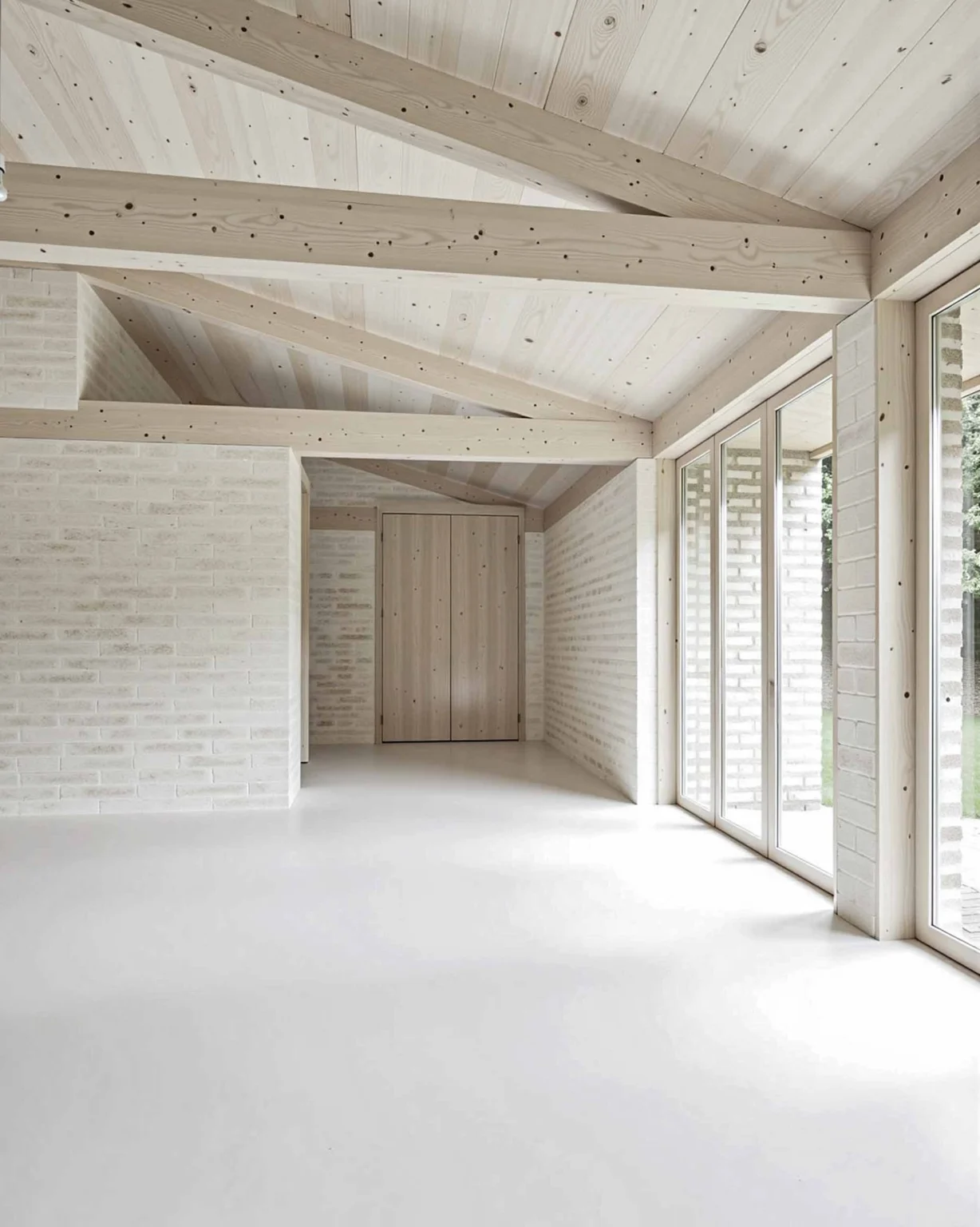 Intérieur rural moderne et contemporain avec plafond en bois clair apparent, murs en briques blanches et grandes baies vitrées, conception architecturale signée Arthur Montessuit, Architecte en Haute-Savoie.