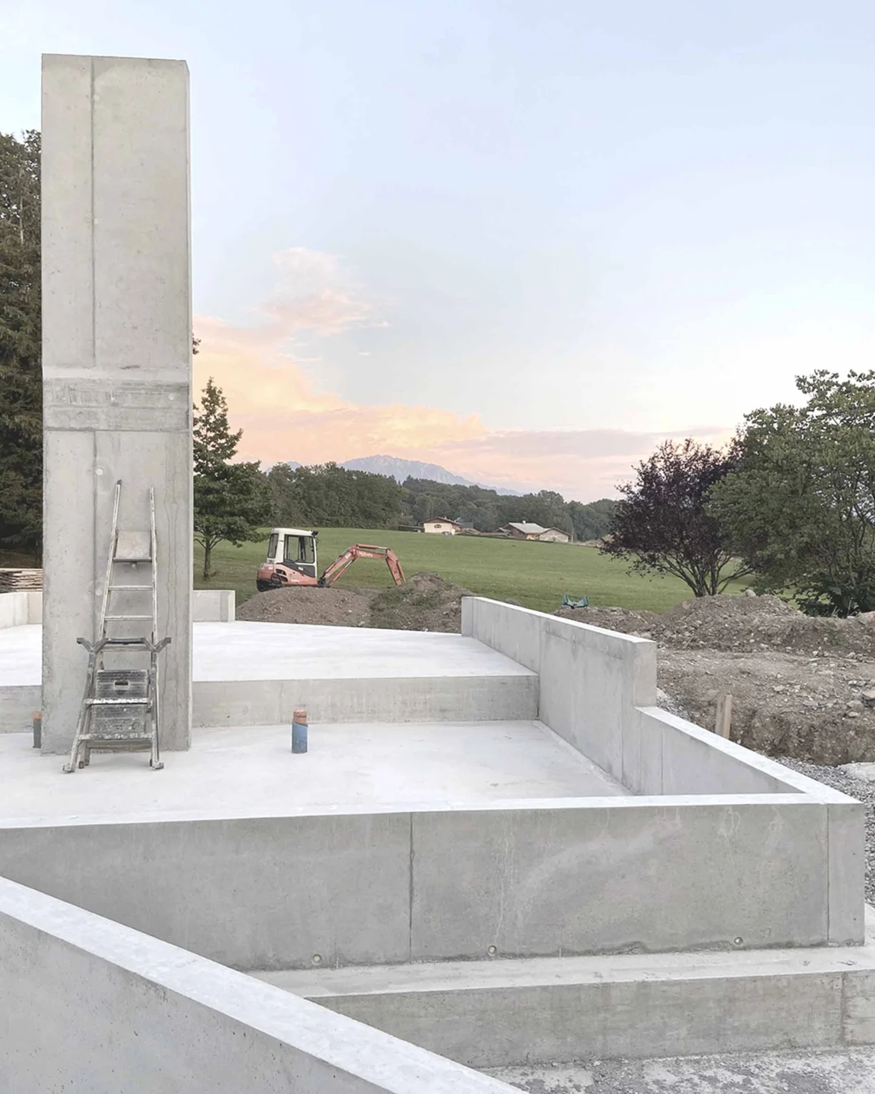 Structure rurale moderne et contemporaine en béton brut avec cheminée et vue sur campagne, conception architecturale par Arthur Montessuit, Architecte en Haute-Savoie.